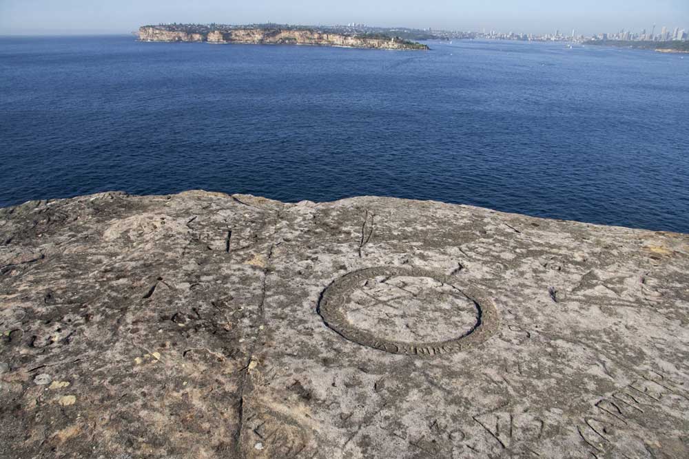 Inscriptions carved near the edge of a cliff at the North Head Quarantine Station with Sydney's skyline in the distance. Credit: copyright Ursula Frederick.