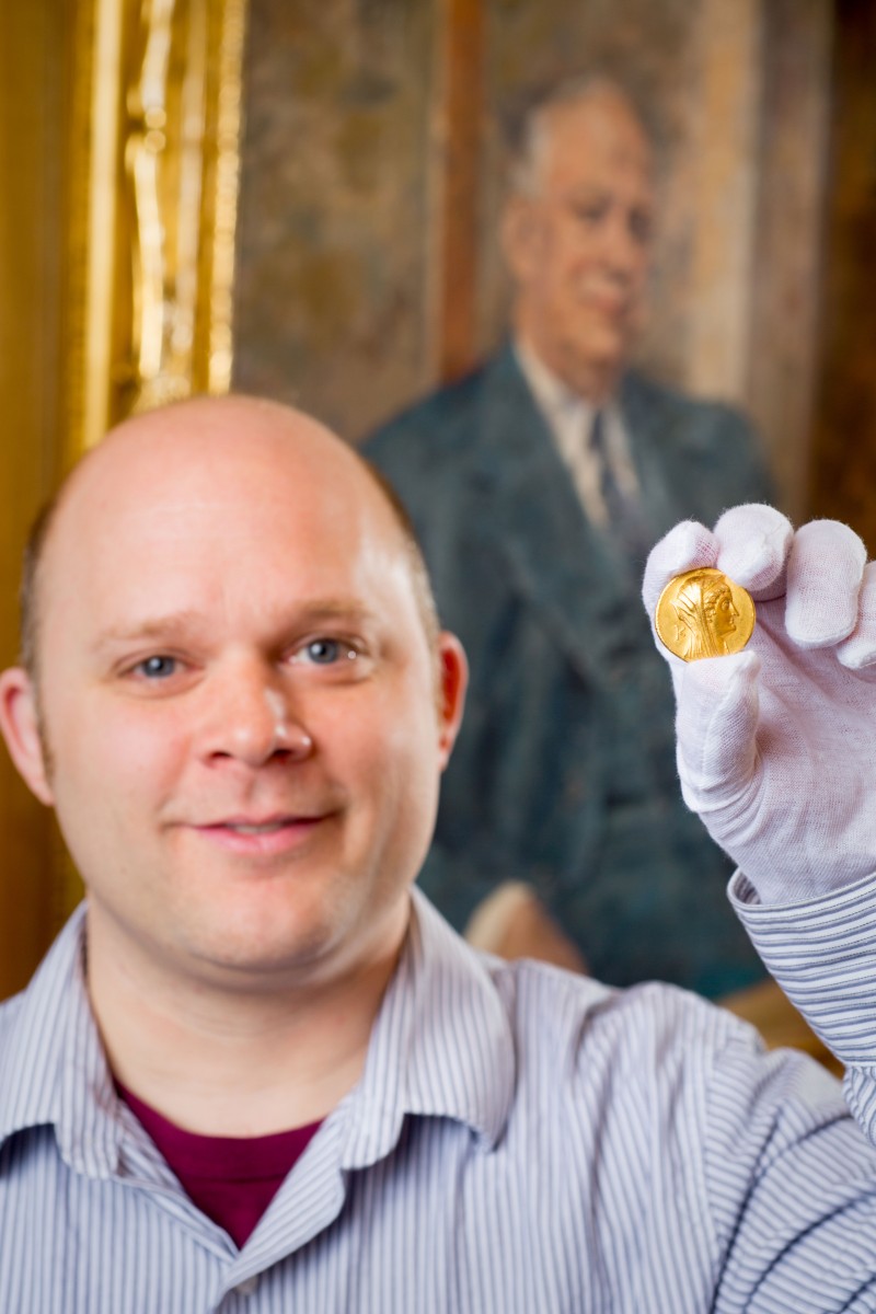 Philip Kiernan, UB assistant professor of classics, holding a Greek coin of Egyptian queen Arsinoe II (285 to 246 B.C.). Photo Credit: Douglas Levere.