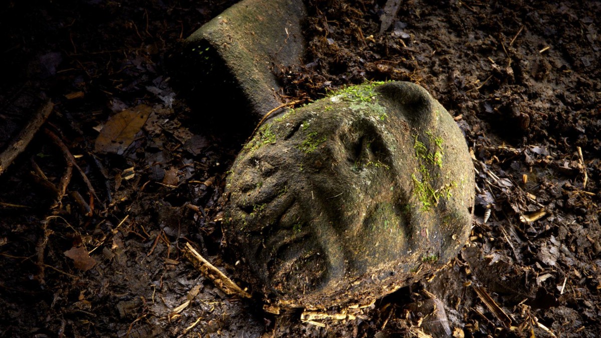 A “were-jaguar” effigy, likely representing a combination of a human and spirit animal, is part of a still-buried ceremonial seat, or metate, one of many artifacts discovered in a cache in ruins deep in the Honduran jungle. Photo Credit: Dave Yoder, National Geographic.