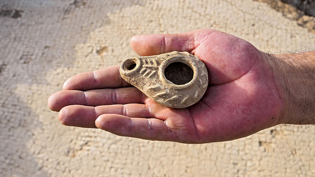 A small oil lamp is held over the mosaic floor of a Byzantine-era church. Photo Credit: Times of Israel /Yonatan Sindel / Flash90.