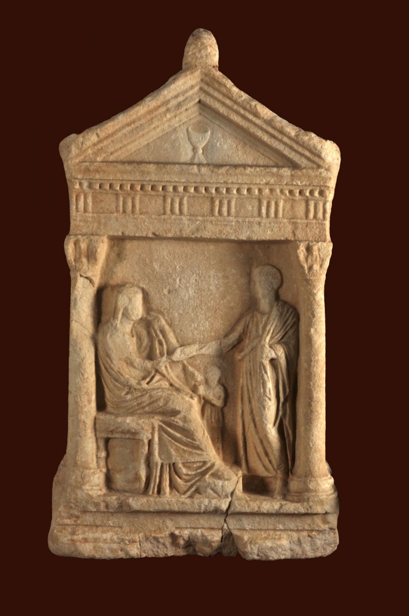 Fig. 32. Marble bas-relief head stone depicting a “banquet” scene. It is shaped like a Corinthian style temple, with Ionian columns and Corinthian capitals supporting a Doric entablature. On the drum of the pediment there is a kylix. 1st c. BC. Chios town. 