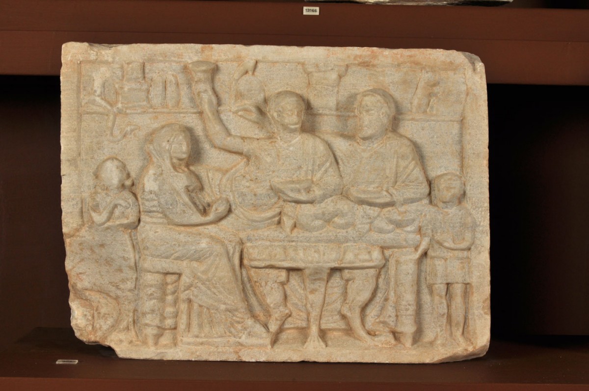 Fig. 34. Marble grave stele in relief depicting a funeral banquet. In the background, behind the banqueters, the dead man’s armaments can be seen (greaves, helmet) and chthonic symbols (snake and horse’s head). 2nd c BC. Pyrgi.