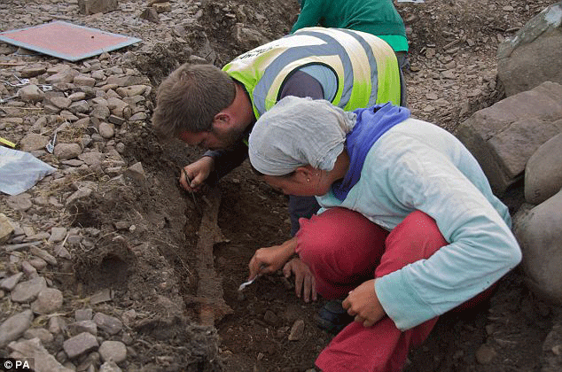 Dr Oliver Harris examines a sword with another archaeologist at the burial site. Photo Credit: Daily Mail.