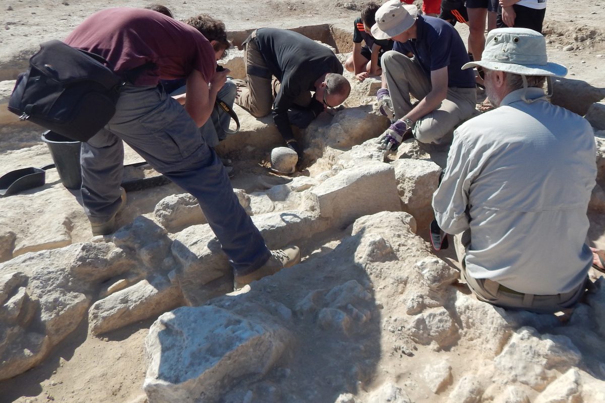 Members of the excavation team and Open Day visitors gather around as archaeologist Donald Clark prepares to lift a complete Roman pot from the spot where it has lain for 1,600 years.