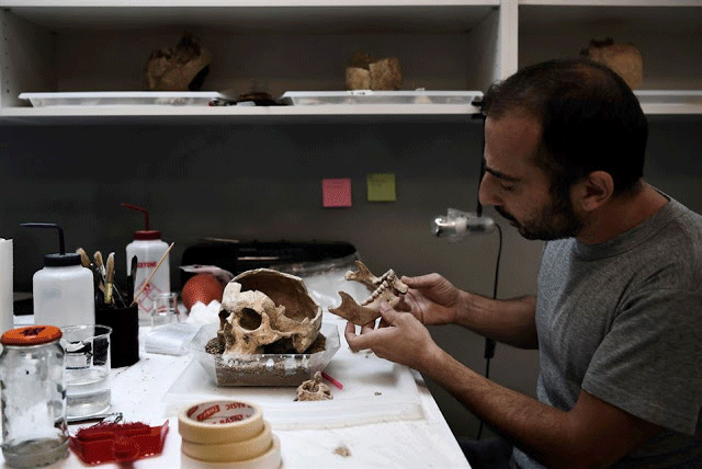 A conservator works on a human skull in a lab at the American School 
of Archaeology in Athens on July 7, 2017. Photo Credit: Aris Messinis/AFP/TANN.