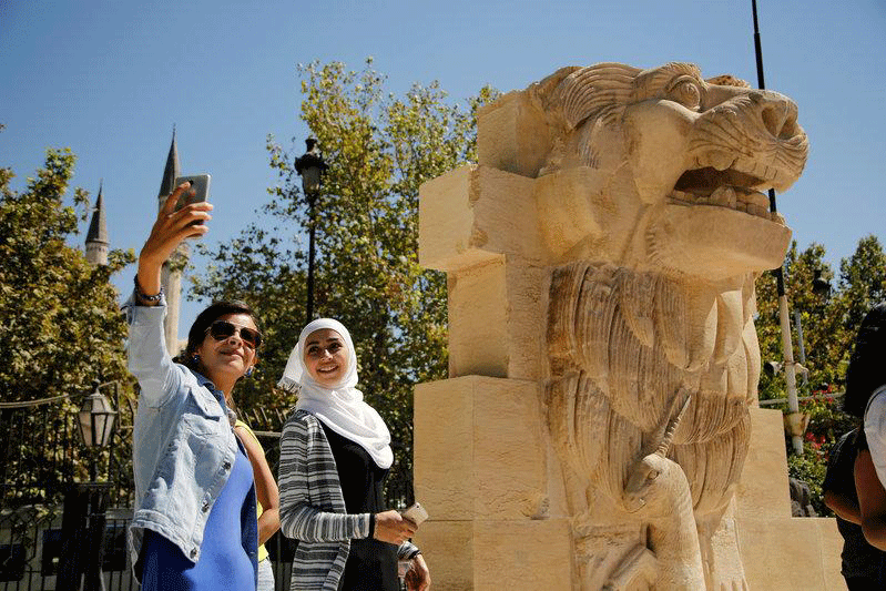 Syrian women take selfies in front of the restored Lion of al-Lat, a 2,000-year old statue, on display in Damascus, Photo Credit: REUTERS/Omar Sanadiki