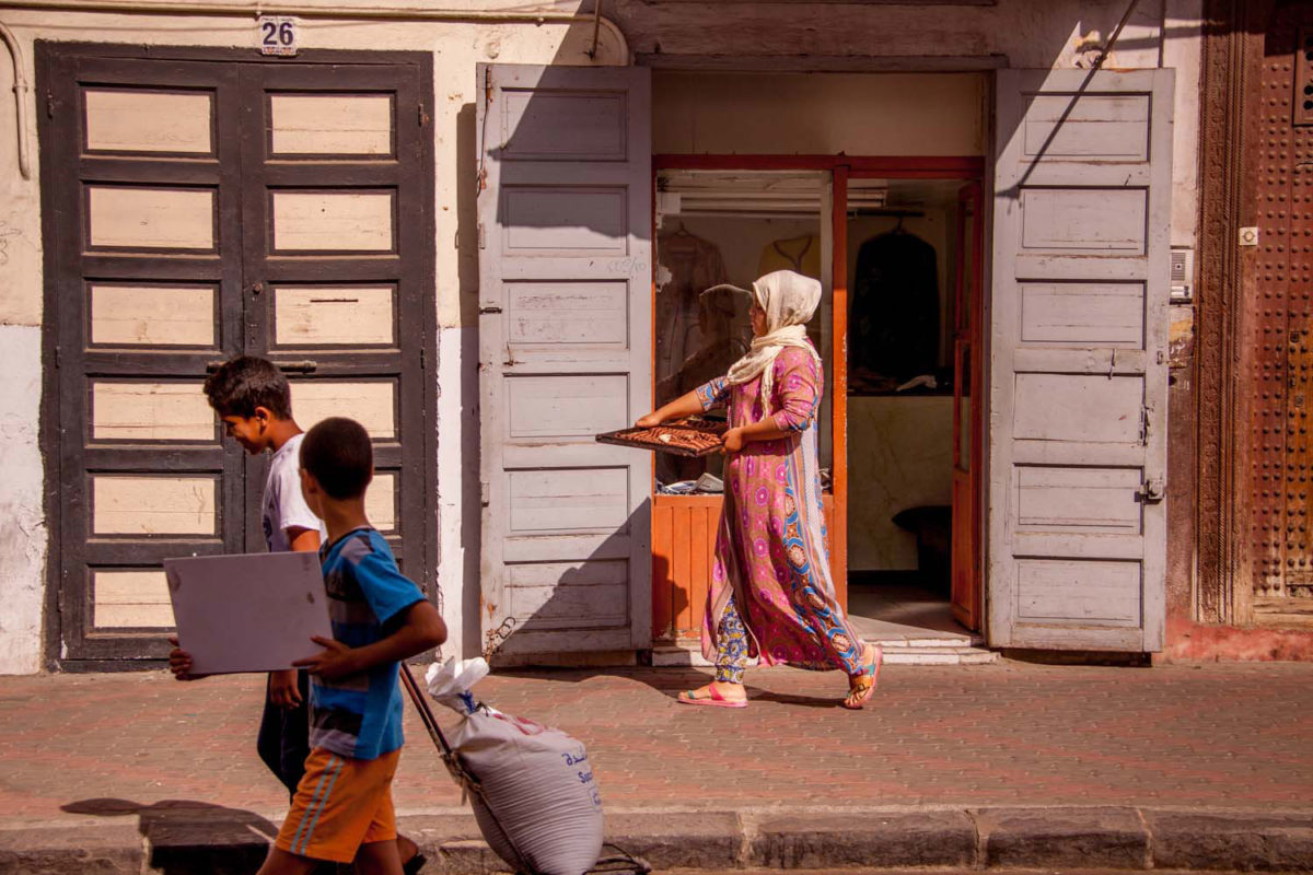 A woman is heading towards a local baker balancing a tray with bread on her head.