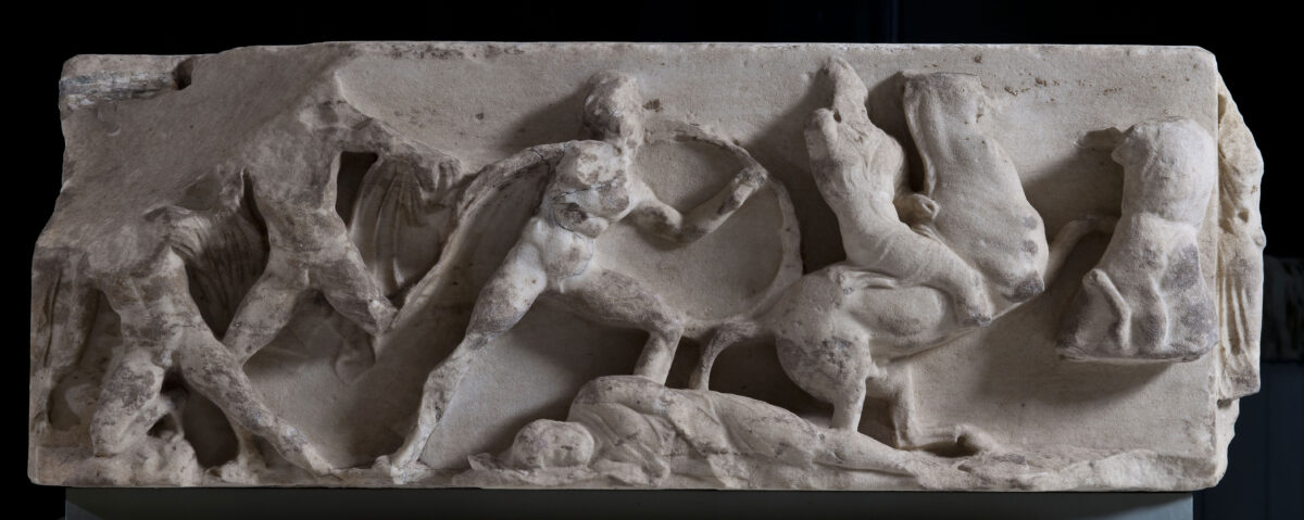 Athena Nike Temple. South frieze. Corner block a (Ακρ. 18135 south side)
The south frieze of the Temple of Athena Nike most probably depicts the Greeks’ victorious battle against the Persians at Marathon in 490 BC, where the Athenians played a leading role. On the left of its south side a Greek hoplite comes in aid of one of his comrades, who falls down after he was hit by the arrow of a Persian archer depicted on the right, at the other side of the block. In the centre, another Greek with a shield in his left hand chases after a Persian horseman while another Persian lies dead on the ground.
