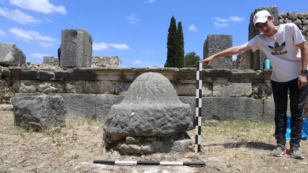 An olive millstone in Volubilis. Research assistant Drew Messing holds a tool for scale. Credit: Jared Benton.