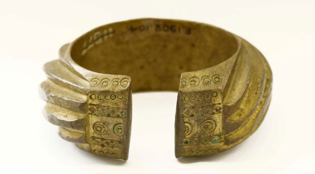 A brass penannular bracelet decorated with heavy slanting bands.