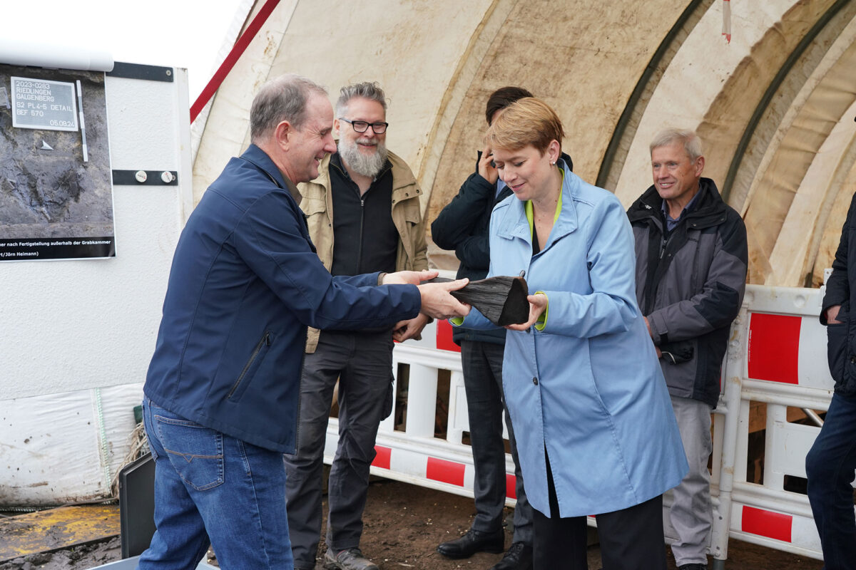 Fig. 4. Ms Andrea Lindlohr MdL, Staatssekretärin at the Baden-Württemberg Ministry for Regional Development and Housing, with the club-like wooden artefact left behind by the Celtic builders. Credit: LAD / Andreas Dubslaff